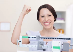 woman raising fist and smiling while standing on a doctors scale