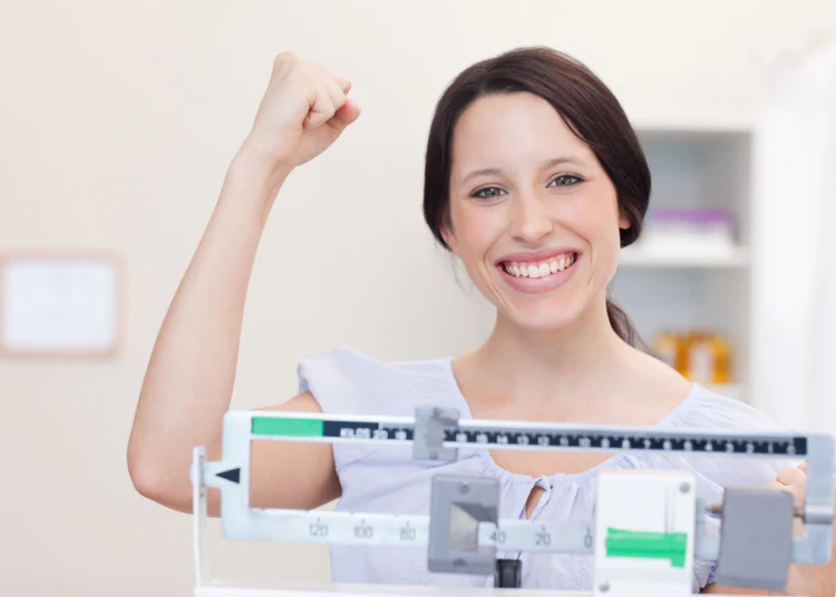 woman raising fist and smiling while standing on a doctors scale