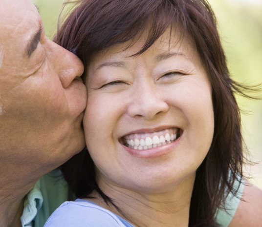 Asian woman smiling being kissed on cheek by asian man