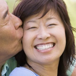 Asian woman smiling being kissed on cheek by asian man