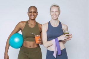 two women in workout clothing with a ball and resistance band